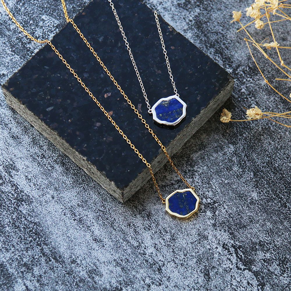 Two bright blue lapis lazuli gemstone necklaces with gold flecks in sterling silver and 14k gold on black stone on stone background